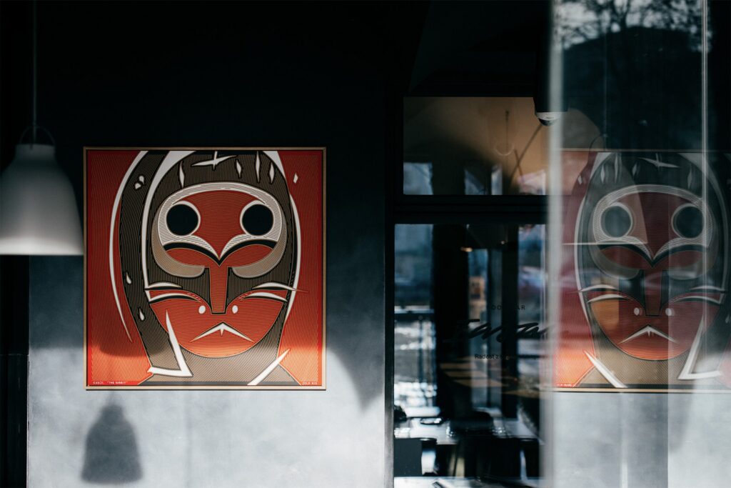 Kanji by Zolo Kis — the red masked portrait displayed on a wall beside a reflective window