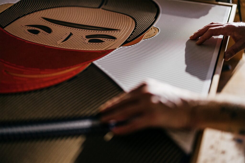 Hariko by Zolo Kis — hands working on the portrait near its wooden frame