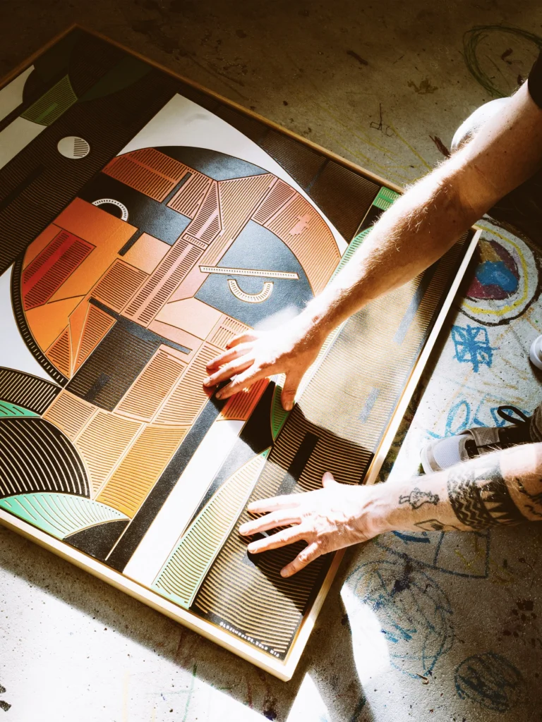 Oldschooler by Zolo Kis — hands working on the framed orange and green portrait on a table