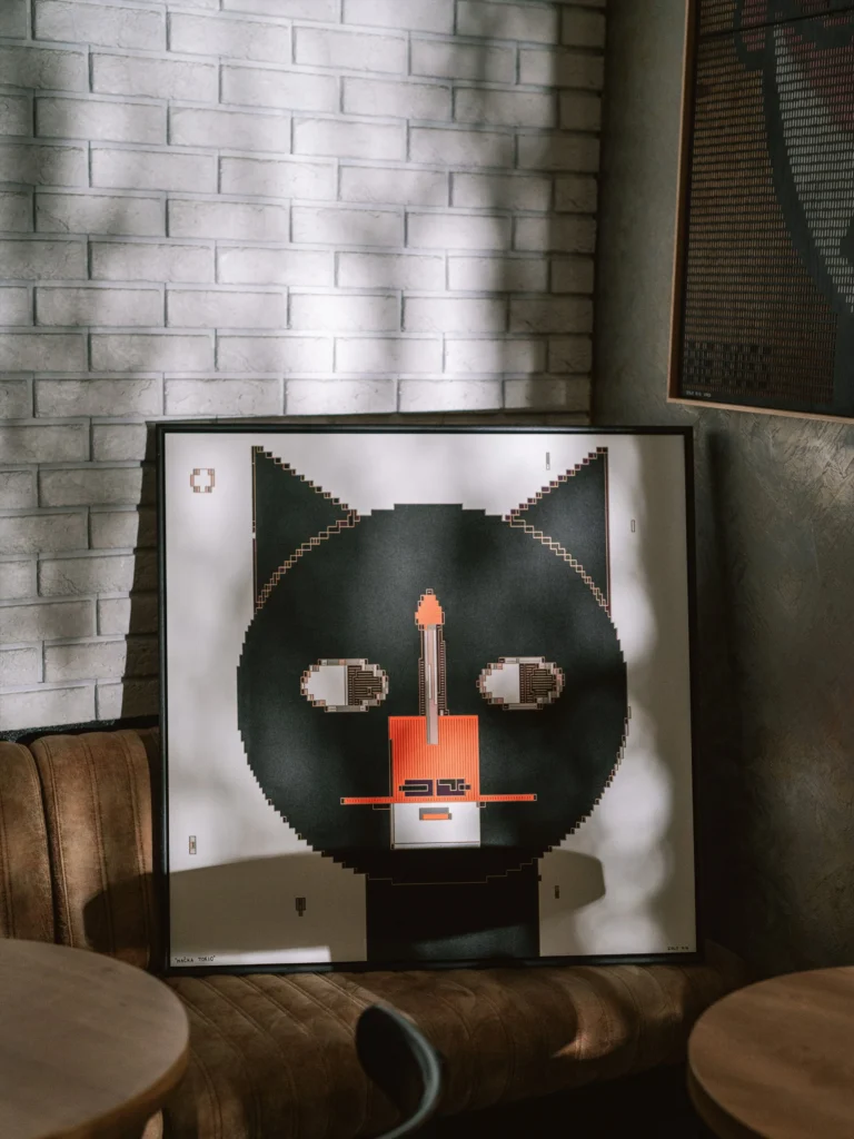 The Cat - Tokio by Zolo Kis — the framed cat portrait resting on a chair beside a white brick wall