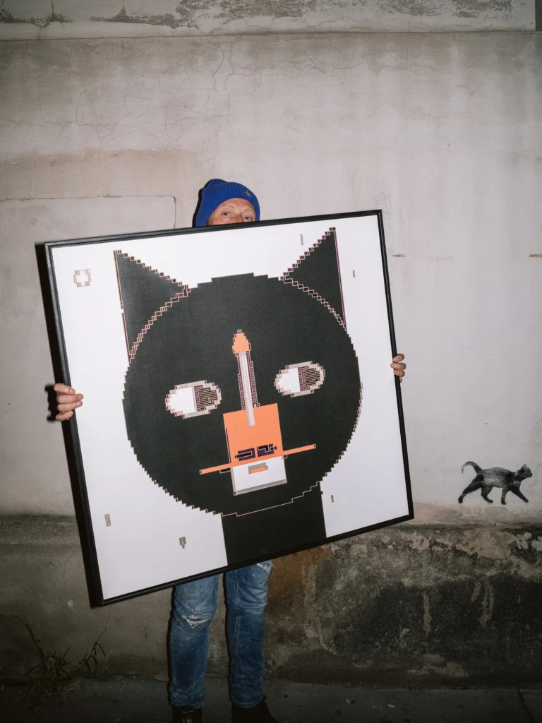 The Cat - Tokio by Zolo Kis — a person holding the framed cat portrait against a concrete wall